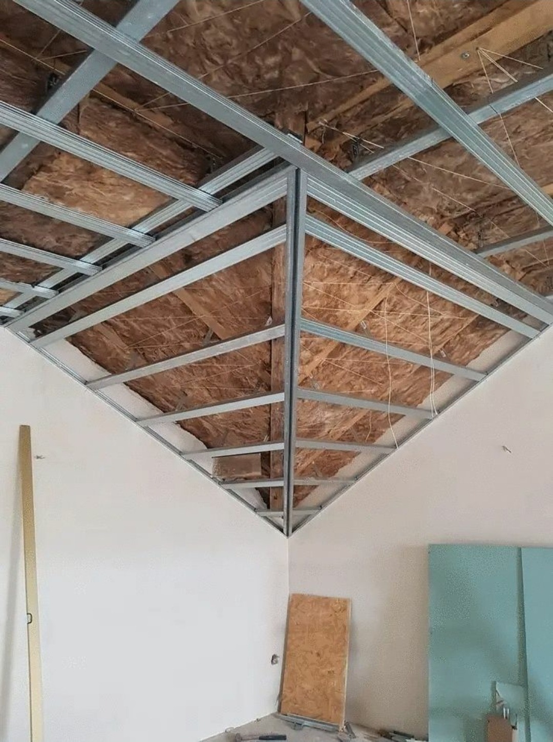 Konstrukcja metalowa sufitu podwieszanego z izolacją wełną mineralną, widok z dołu, fragment ściany i narzędzi na podłodze.