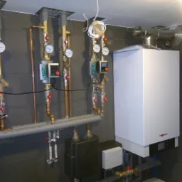 Nowoczesna kotłownia z białym piecem gazowym Viessmann, miedzianymi rurami i szarą płytką na ścianie, widoczne manometry i elektroniczne sterowniki Wilo.