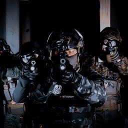 pietruszka tworzy - Trzech zamaskowanych mężczyzn w taktycznym ekwipunku celuje bronią w ciemności, oświetleni punktowo, z logo 'HEVY AIRSOFT' na środkowym planie.
