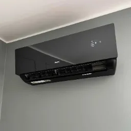 Czarny klimatyzator AUX zamontowany na szarej ścianie, wyświetlacz pokazuje temperaturę 16 stopni Celsjusza.