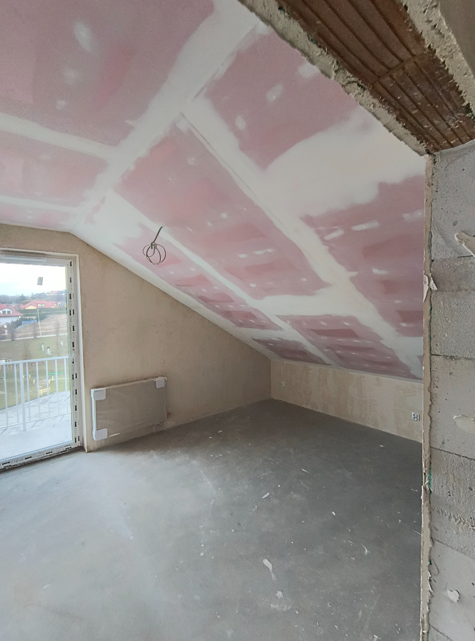 Poddasze w trakcie prac wykończeniowych: widoczne płyty karton-gips na skosach sufitu, łączenia szpachlowane, surowa ściana z pustaków i okno balkonowe.