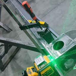 MK TECHNIKA MICHAŁ KASZA - Ustawianie metalowej konstrukcji za pomocą poziomicy laserowej DeWalt, widoczny zacisk śrubowy i poziomica.