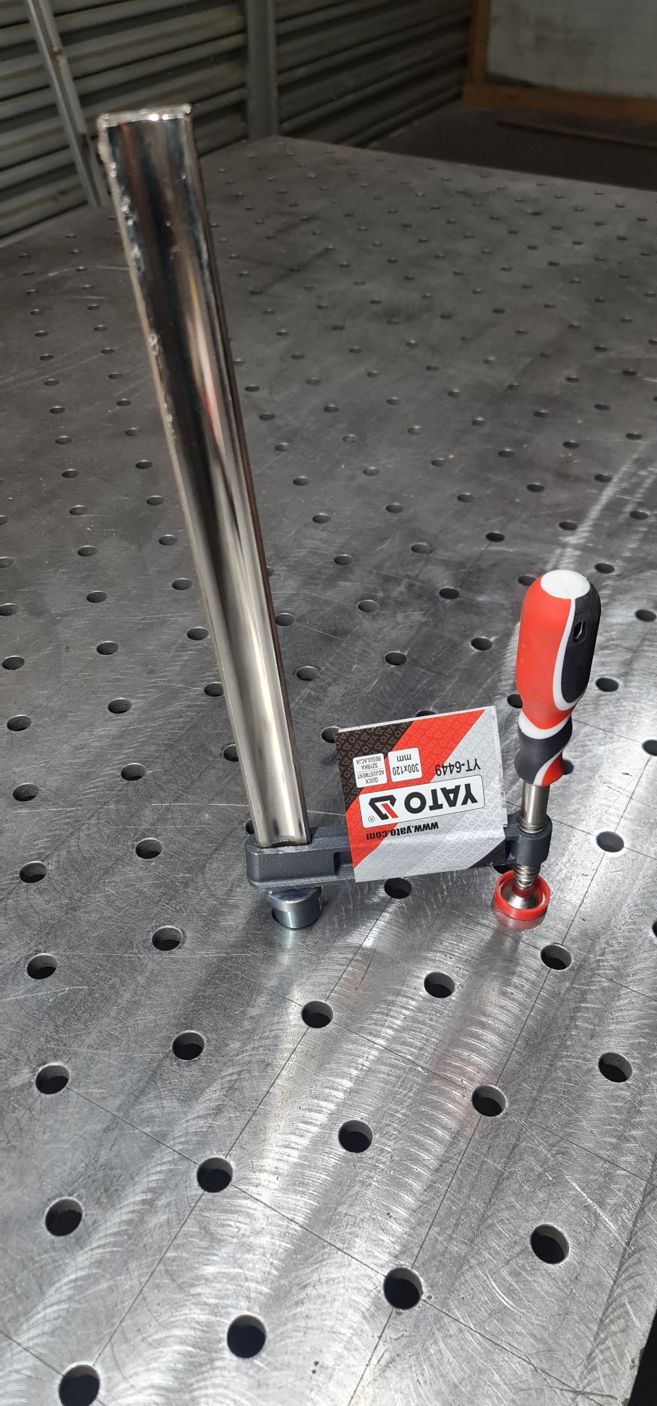 Metalowa rura zamocowana na stole spawalniczym za pomocą zacisku śrubowego marki Yato.