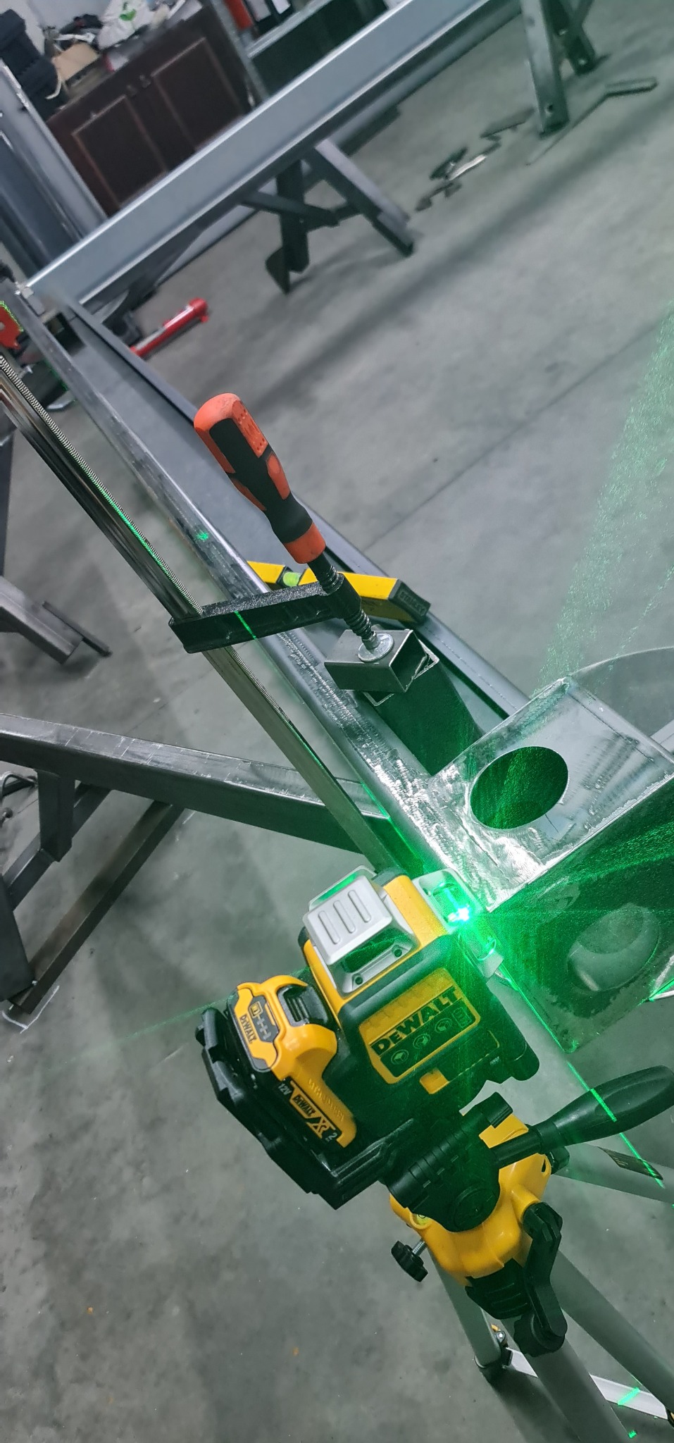 Ustawianie metalowej konstrukcji za pomocą poziomicy laserowej DeWalt, widoczny zacisk śrubowy i poziomica.