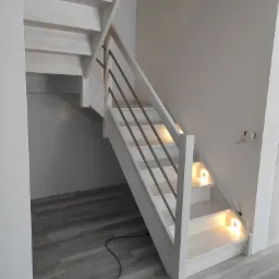 Białe drewniane schody z metalową balustradą i podświetleniem LED na stopniach, widok z dołu.