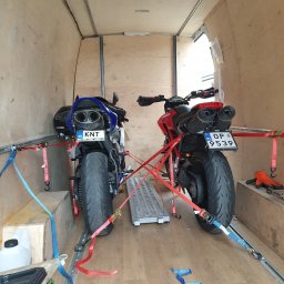 FHU B.R.Trans Ryszard Szmyglewski - Dwa motocykle, czerwony Ducati i niebieski Yamaha, zabezpieczone pasami wewnątrz drewnianej furgonetki, gotowe do transportu. Widoczne tablice rejestracyjne i rampy najazdowe.