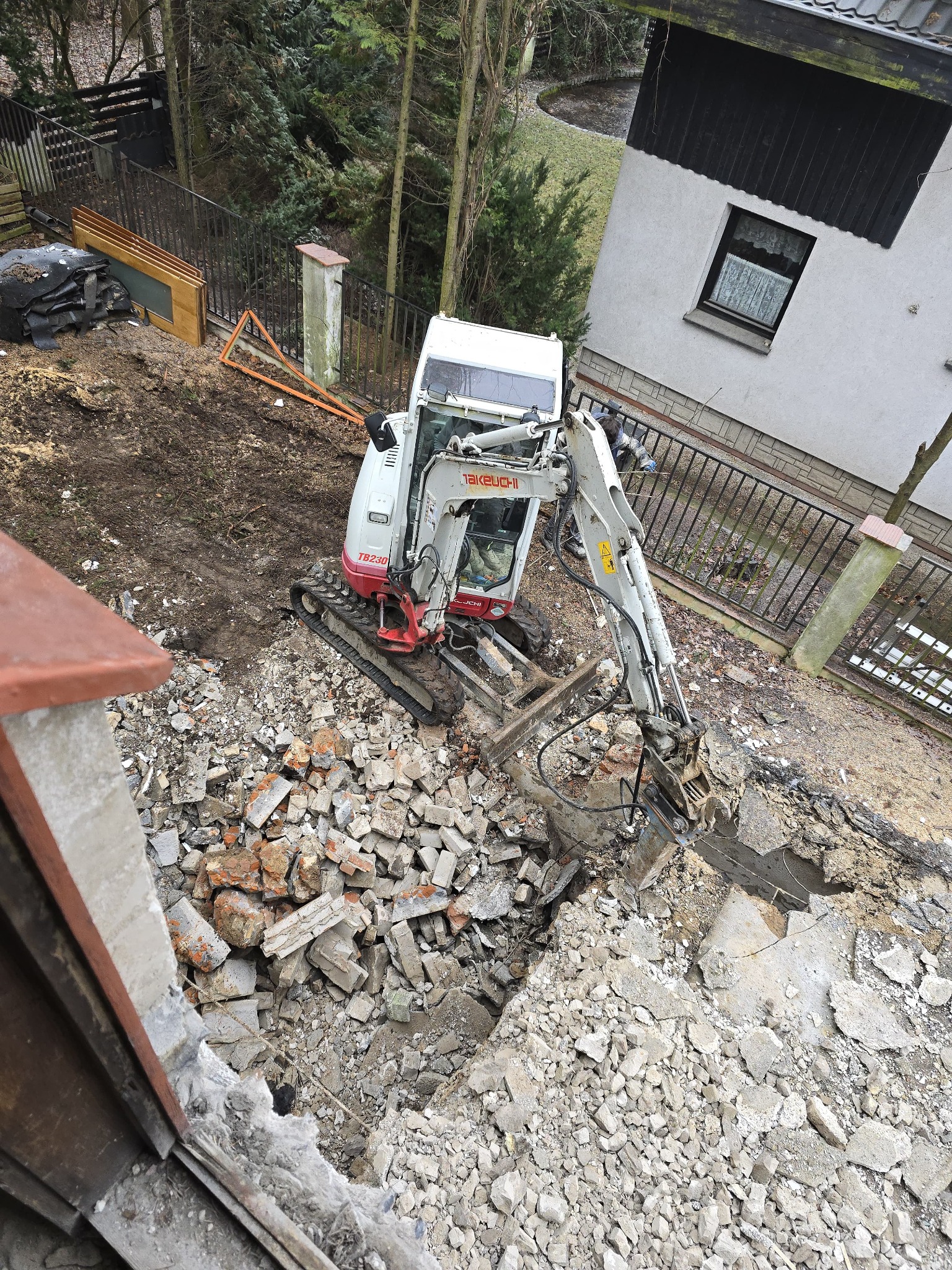 Mini koparka Takeuchi TB230 kruszy beton na placu budowy z widokiem z góry, gruzowisko i teren przygotowany pod dalsze prace.