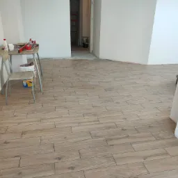 Układanie drewnopodobnych płytek podłogowych w Iławie, widoczny stół roboczy z narzędziami glazurniczymi i częściowo otwarte drzwi do kolejnego pomieszczenia.