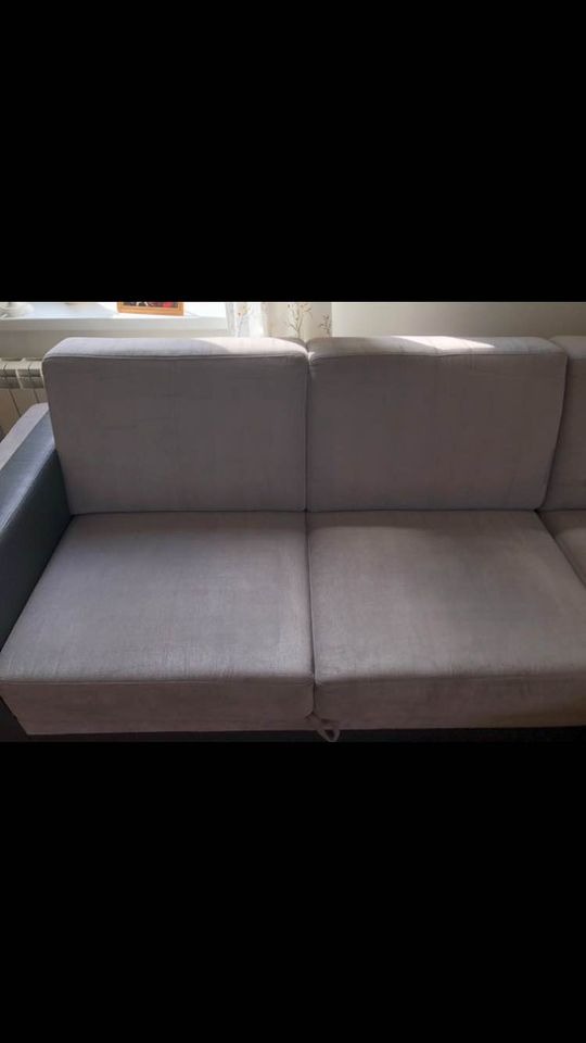 Szara, modułowa sofa z tapicerką o widocznej fakturze, sfotografowana w dziennym świetle padającym z okna, z fragmentem grzejnika w tle.