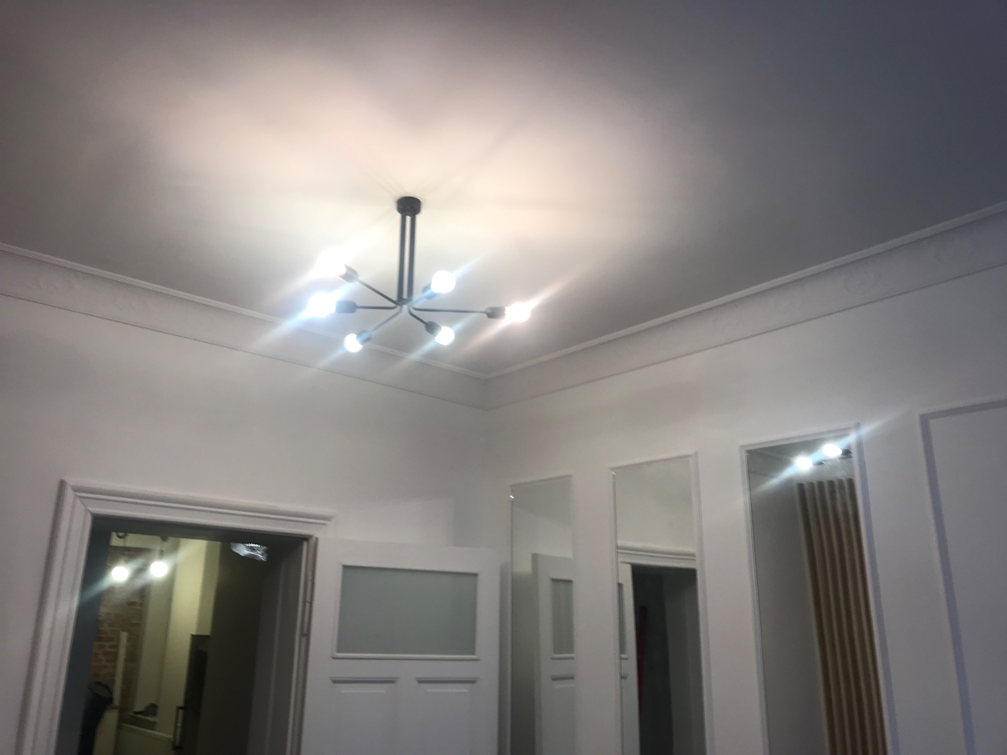 Białe wnętrze z nowoczesną lampą sufitową, sztukaterią i lustrami w wąskich ramach.