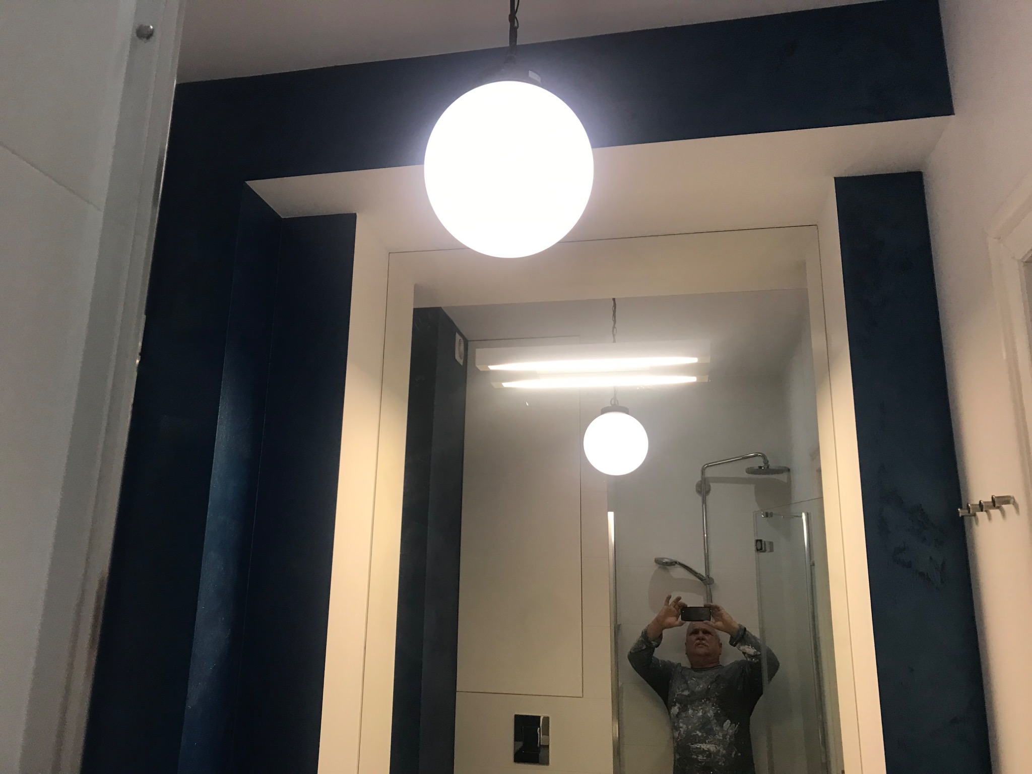 Łazienka po malowaniu w odcieniach granatu, widoczne odbicie malarza robiącego zdjęcie telefonem, okrągła lampa sufitowa.