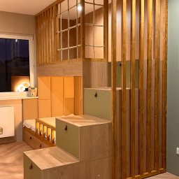 Cool-Ka MEBLE - Pokój dziecięcy z drewnianym łóżkiem na antresoli, schodami pełniącymi funkcję szafek z oliwkowymi frontami i dekoracyjną ścianką z pionowych listew; na podłodze dywanik z motywem pojazdów.