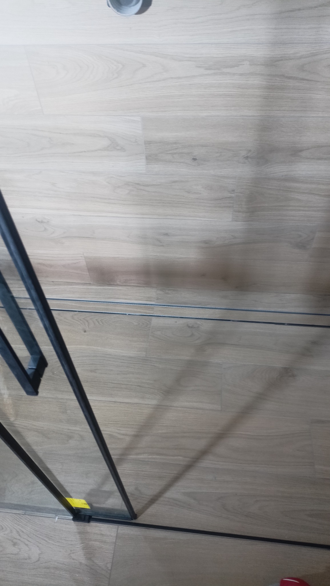 Fragment kabiny prysznicowej z czarnymi profilami na podłodze imitującej drewno, widoczny silikon uszczelniający.