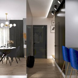 LS Interiors - Nowoczesne wnętrze mieszkania z drewnianą podłogą, widok na jadalnię z okrągłym stołem i krzesłami oraz na korytarz z czarnymi drzwiami i niebieskimi hokerami przy wyspie kuchennej.