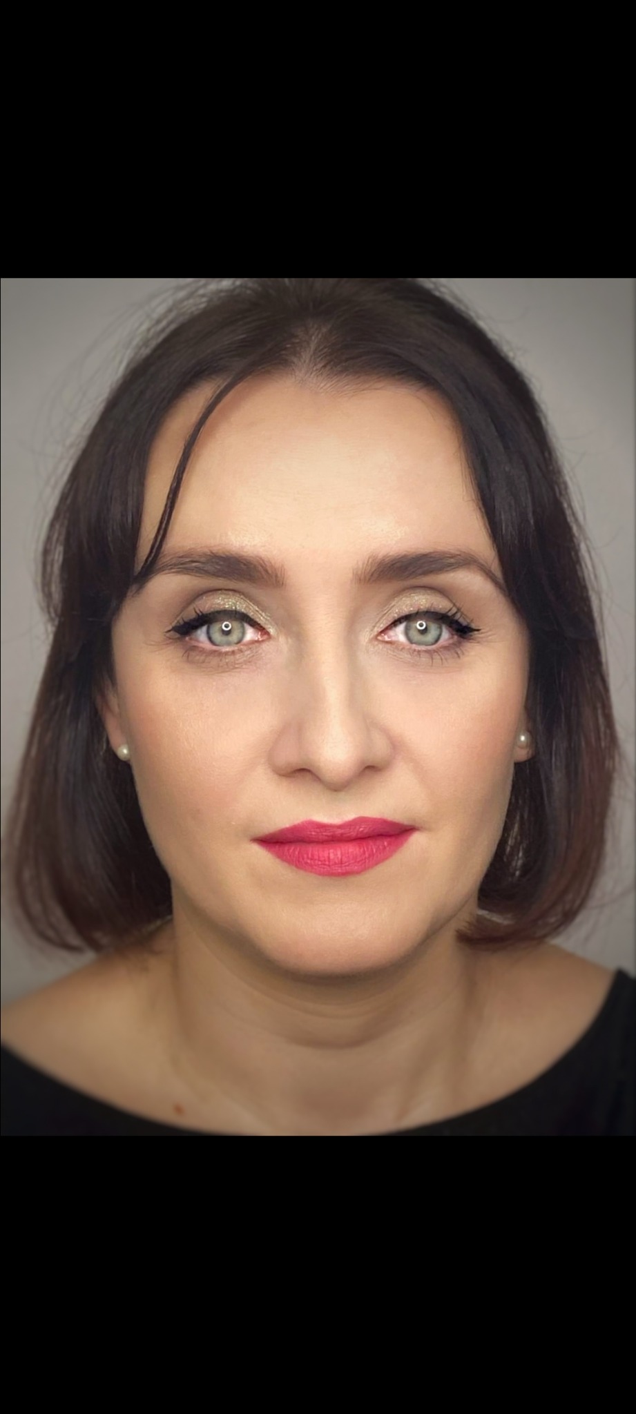 Portret kobiety z delikatnym, złotym makijażem oczu, czarną kreską i intensywnie różowymi ustami, uzupełniony o perłowe kolczyki.