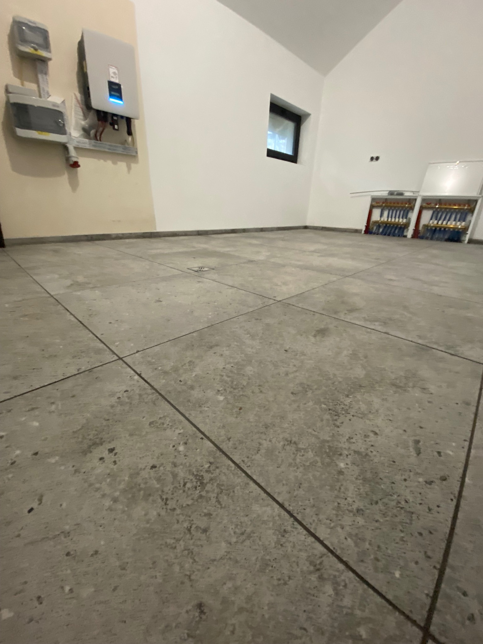 Wykończona podłoga z szarych płyt w nowym pomieszczeniu z instalacją elektryczną i ogrzewaniem podłogowym.