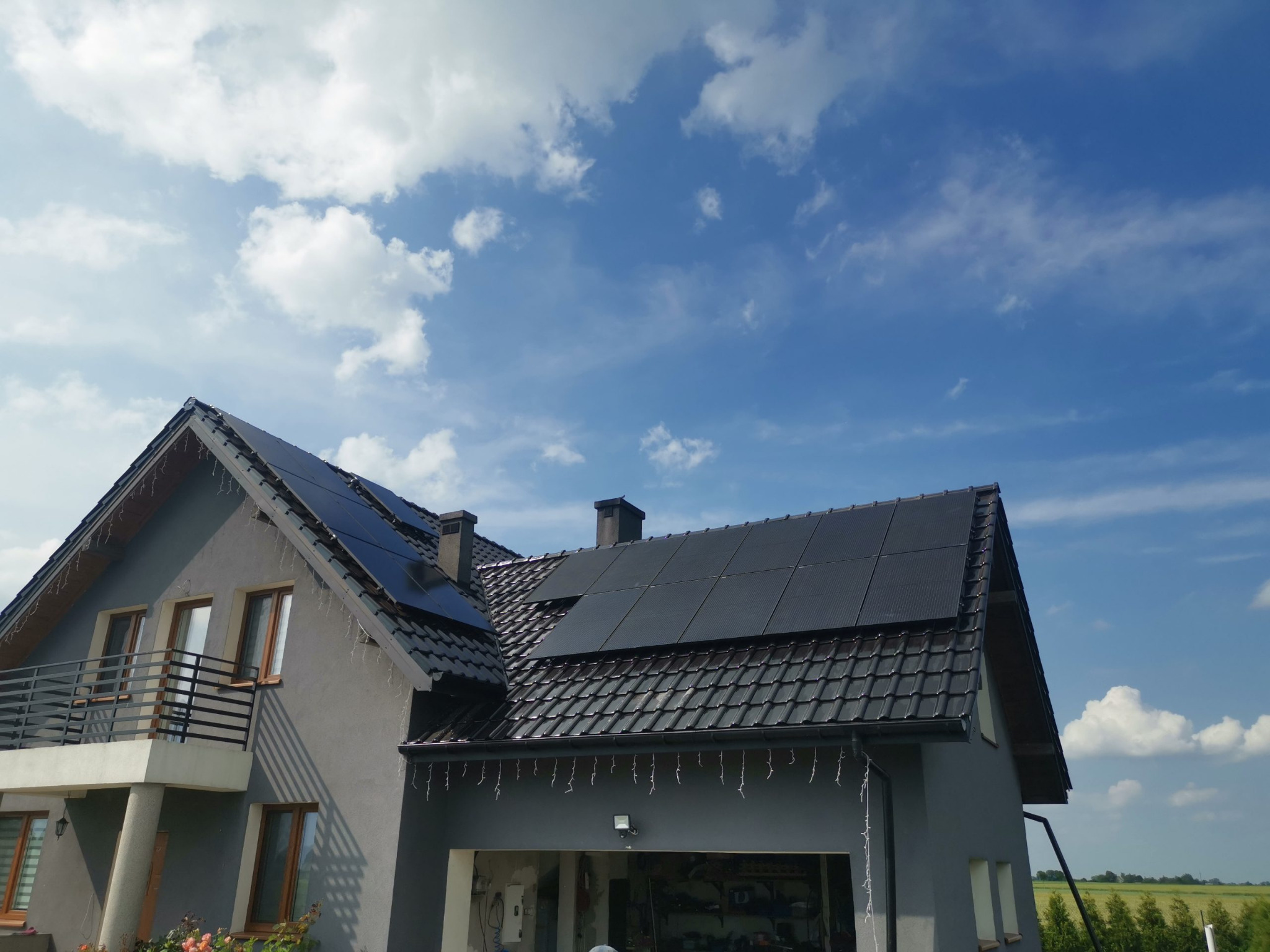 Dom jednorodzinny z zainstalowanymi panelami fotowoltaicznymi na dachu pokrytym czarną dachówką, widoczne dekoracyjne lampki zwisające z okapu.