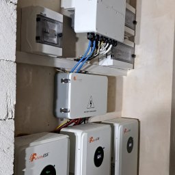 Doradca ds. OZE - fotowoltaika/pompy ciepła - Instalacja magazynów energii Felicity ESS z podłączonym inwerterem i skrzynką bezpiecznikową na ścianie z surowego betonu. Widoczne kable i rury.