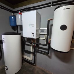 Doradca ds. OZE - fotowoltaika/pompy ciepła - Zestaw urządzeń grzewczych: pompa ciepła Ecodan, dwa zbiorniki Kospel, instalacja rurowa w pomieszczeniu technicznym. Widoczne zawory i manometry.