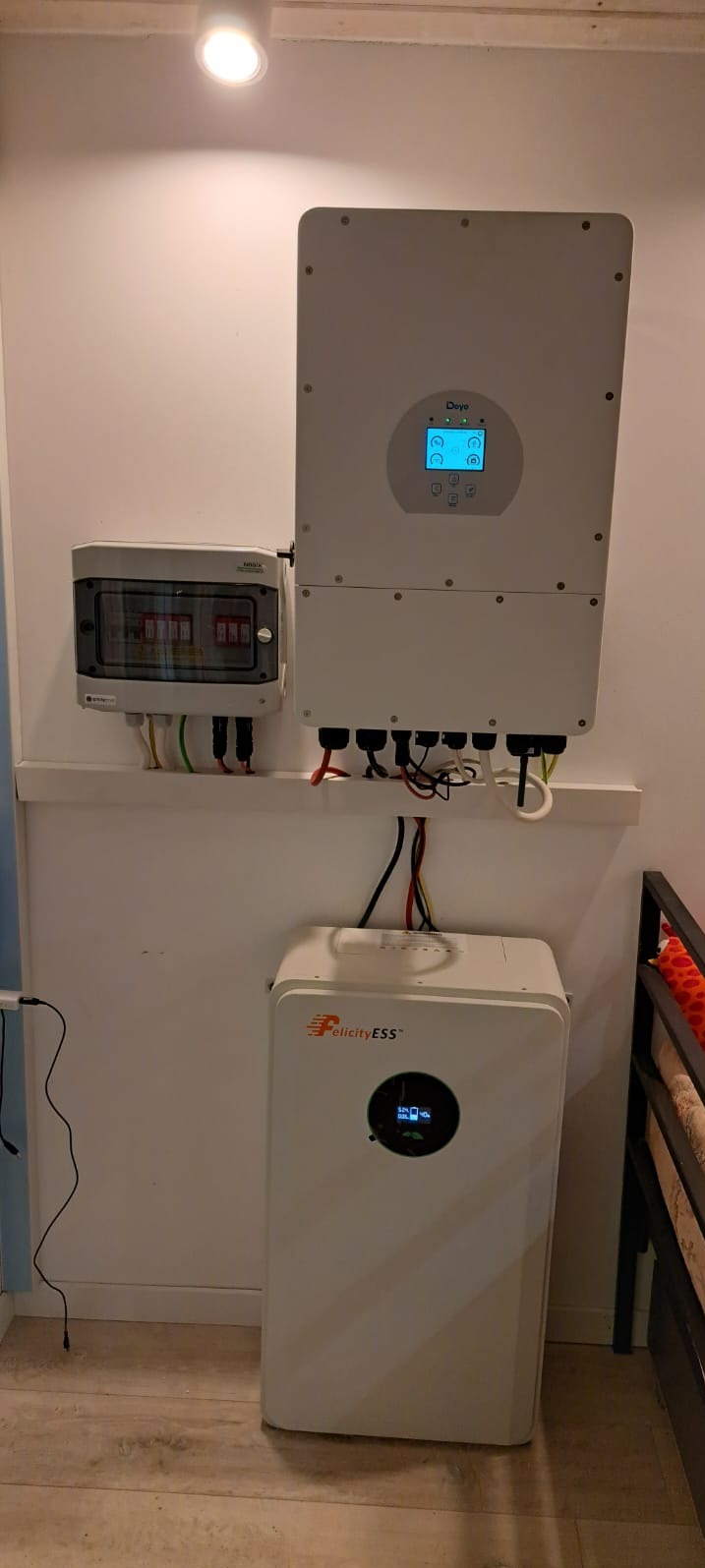 Biały inwerter Deye i magazyn energii Felicity ESS zamontowane na ścianie, z widoczną skrzynką bezpiecznikową i okablowaniem. Instalacja wewnątrz budynku.