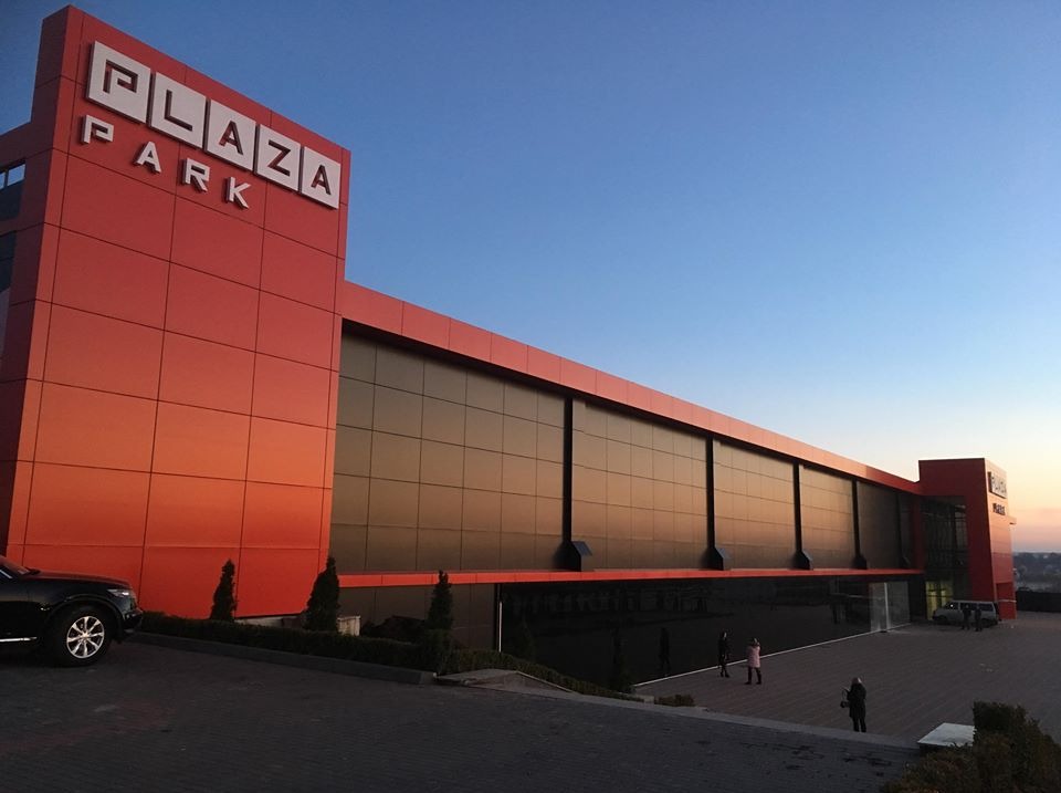 Nowoczesny budynek biurowy Plaza Park z dużą fasadą szklaną i czerwonymi panelami, widok z zewnątrz o zmierzchu.