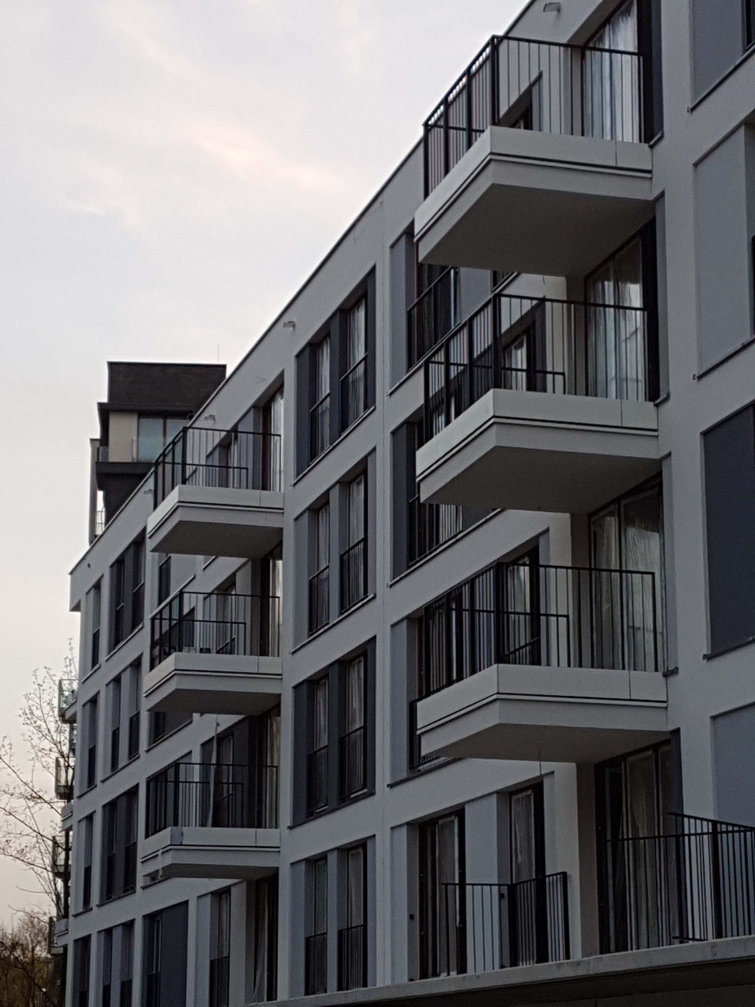 Nowoczesny budynek mieszkalny w Krakowie z balkonami zabezpieczonymi czarnymi, metalowymi balustradami. Widok z dołu, ukazujący powtarzalność elementów architektonicznych.