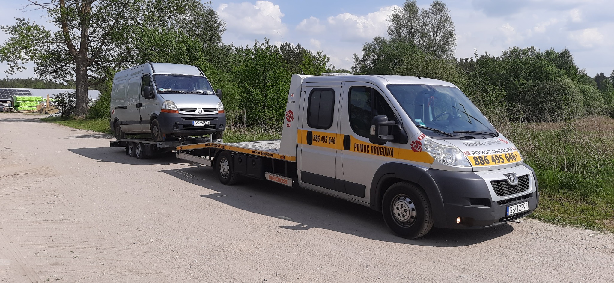 Srebrny van Renault Master przewożony na platformie lawety holowniczej marki Peugeot na żwirowej drodze. W tle widoczne drzewa i zabudowania.