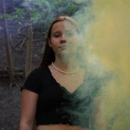 Klaudia Jadczak - Młoda kobieta z perłowym naszyjnikiem pozuje w lesie, otoczona kolorowym dymem, z delikatnym oświetleniem słonecznym w tle.