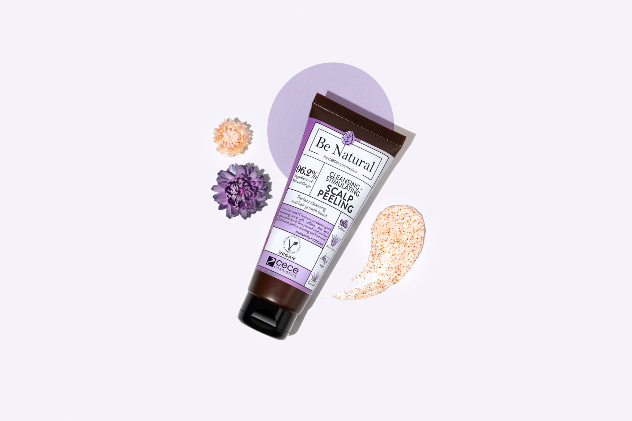 Tubka peelingu do skóry głowy Be Natural na białym tle z kwiatami i próbką produktu, okrągły fioletowy element w tle.