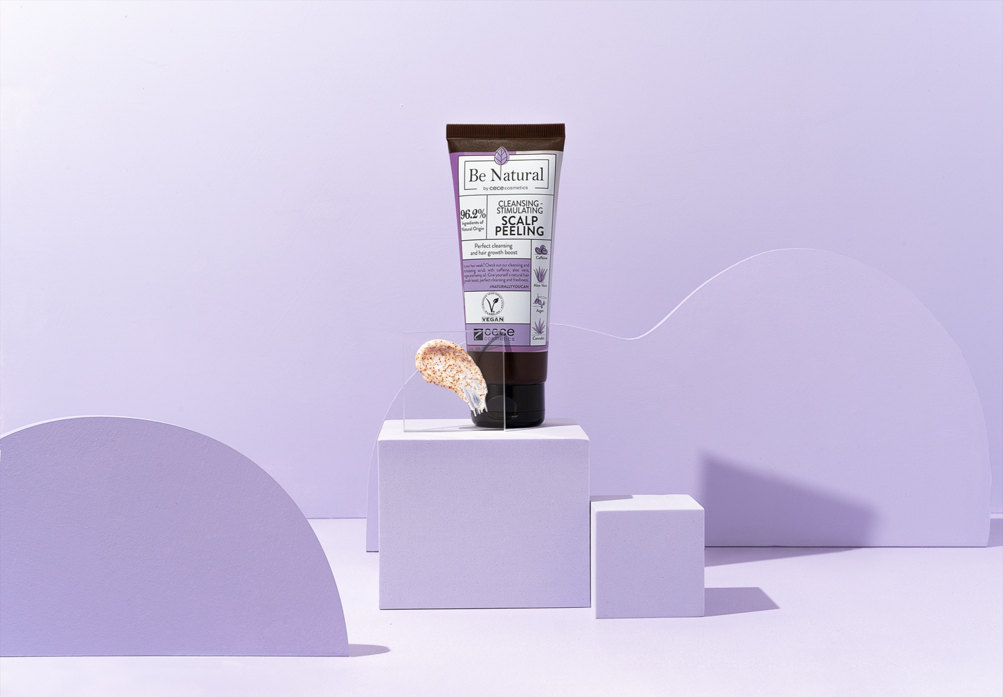 Zdjęcie tuby peelingu do skóry głowy Be Natural by Cece Cosmetics na fioletowym tle z geometrycznymi rekwizytami, prezentacja produktu z widoczną teksturą peelingu.