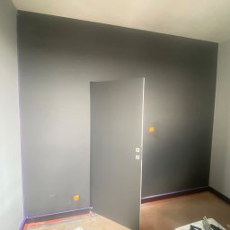 ARP-BUD Artur Pawlak - Pokój po malowaniu, ściany w odcieniach szarości, zabezpieczone taśmą malarską krawędzie, widoczne puszki elektryczne, częściowo otwarte drzwi.