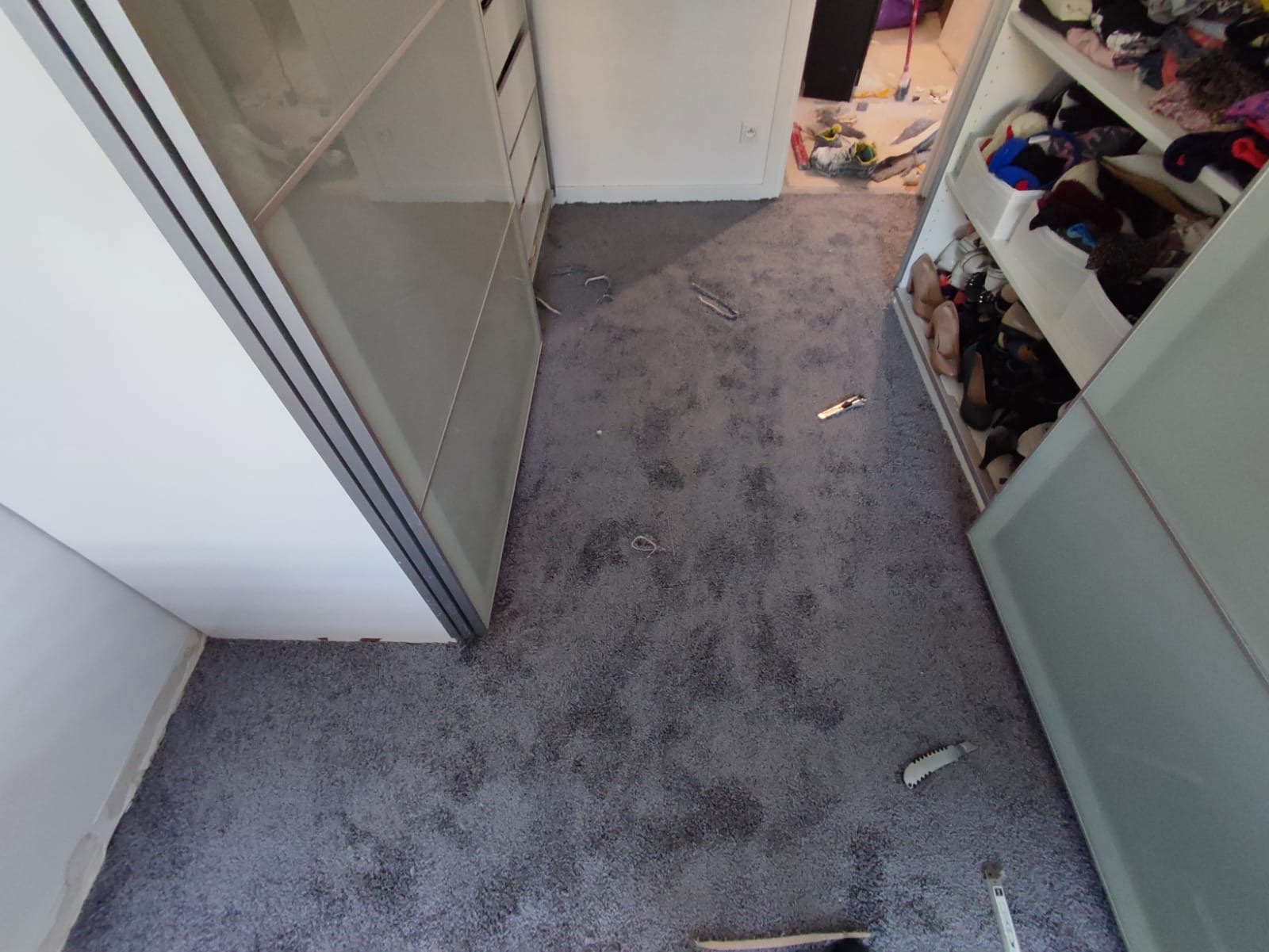 Szara wykładzina dywanowa w pokoju z otwartymi szafami wnękowymi, widoczne narzędzia i resztki po montażu.