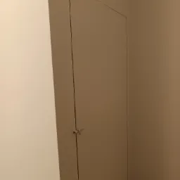 Ukryte drzwi do schowka na poddaszu z zamkiem baskwilowym, wtopione w ścianę pomalowaną na jednolity kolor.