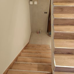 Renovation Usługi Remontowo-Budowlane Krystian Pajek - Wykończone schody drewniane z metalowymi listwami zabezpieczającymi krawędzie, widok z góry, na ścianie widoczne puszki elektryczne i dwie tuby kleju silikonowego.