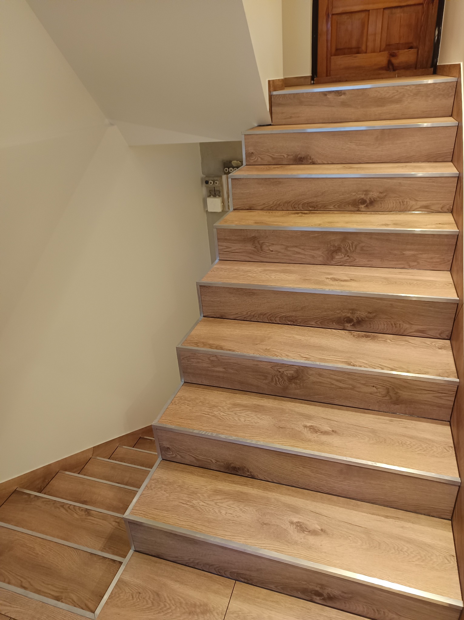 Schody wewnętrzne wyłożone panelami imitującymi drewno, z aluminiowymi profilami zabezpieczającymi krawędzie stopni.