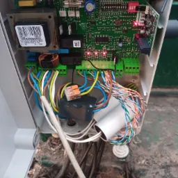 Otwarta obudowa sterownika z widoczną płytką drukowaną, transformatorem i licznymi przewodami podłączonymi do zielonych złączek, z pomarańczową złączką WAGO na jednym z przewodów.