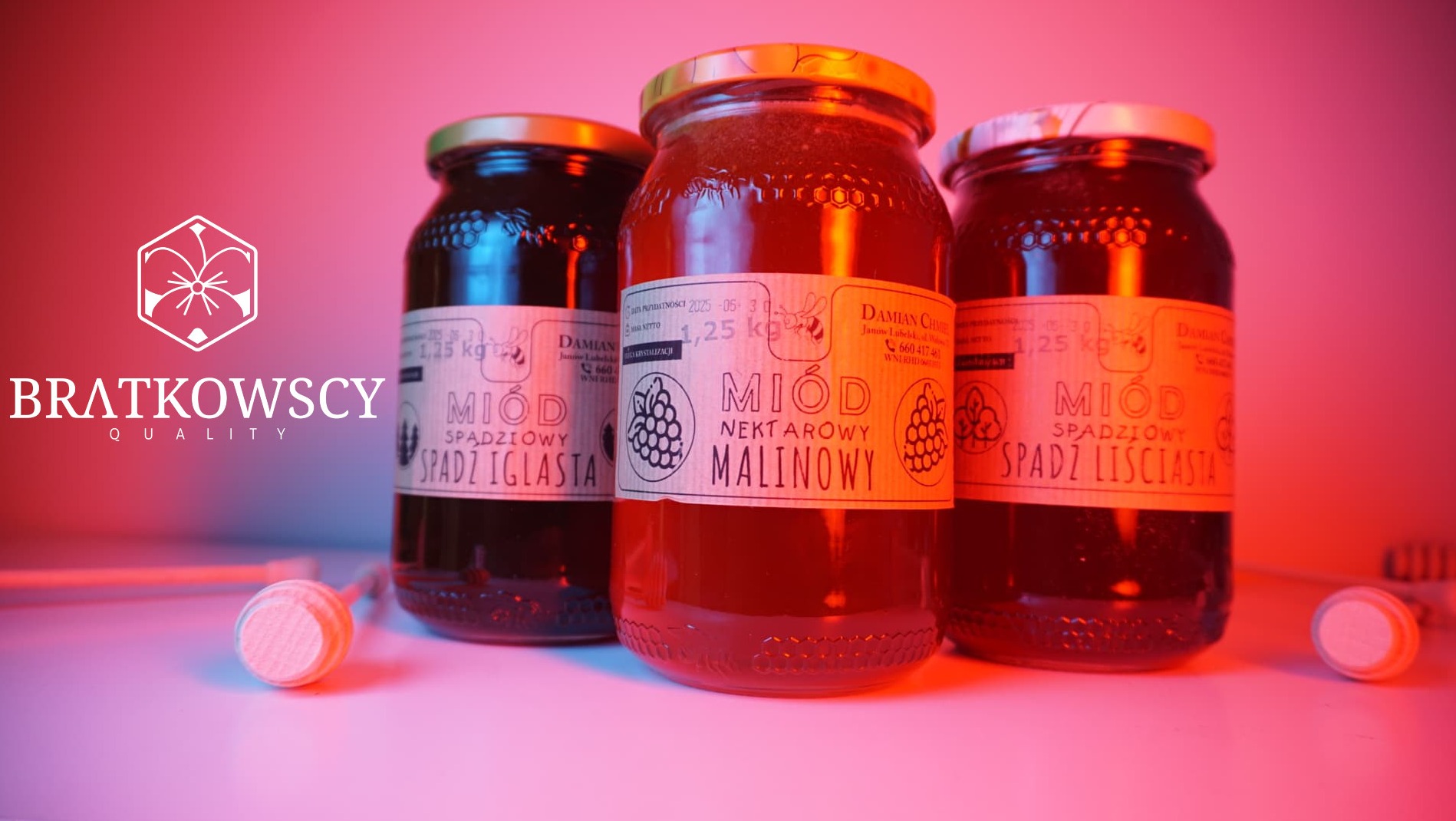 Trzy słoiki z różnymi rodzajami miodu (spadziowy iglasty, nektarowy malinowy, spadziowy liściasty) na białym tle z logo firmy Bratkowscy Quality, oświetlone czerwonym światłem.