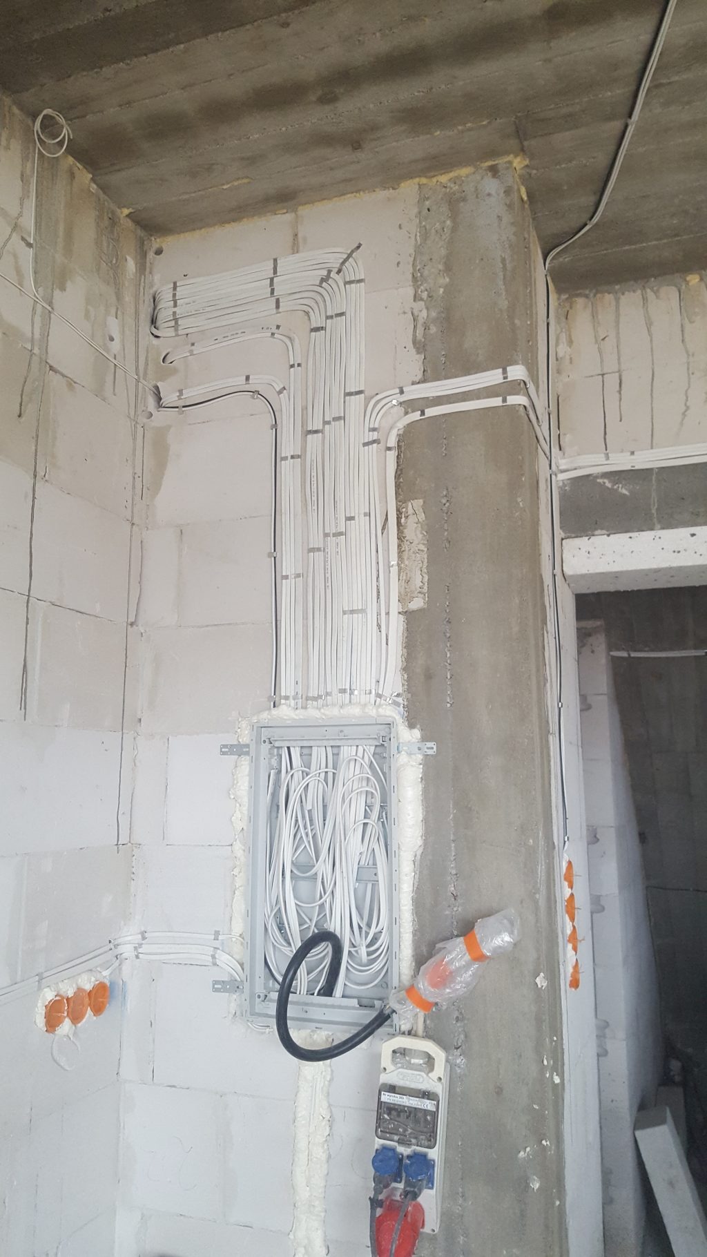Rozprowadzenie instalacji elektrycznej w surowym wnętrzu, widoczne kable w listwach mocowanych do ściany z betonu komórkowego, puszka rozdzielcza oraz przedłużacz z zabezpieczeniem...