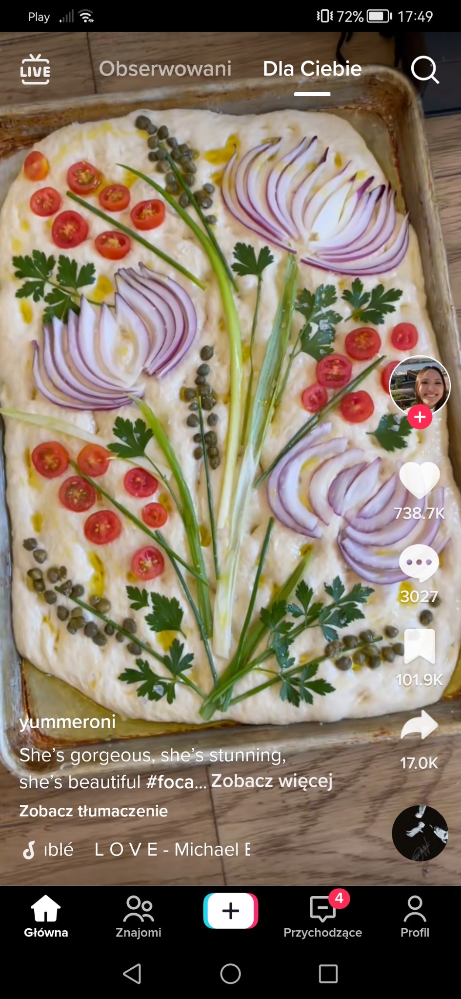 Focaccia udekorowana pomidorkami cherry, cebulą, kaparami i natką pietruszki ułożonymi w kwiatowy wzór, polana oliwą, pieczona w prostokątnej formie.