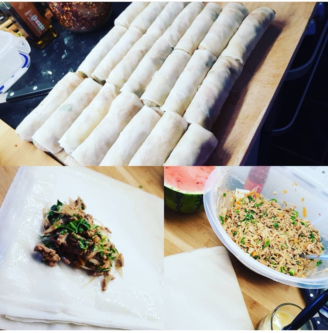 Przygotowanie sajgonek: rząd gotowych zawiniątek na drewnianej desce, farsz na papierze ryżowym i miska z gotowym farszem z warzywami i mięsem, obok arbuz.