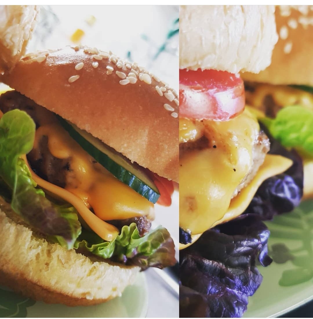 Dwa burgery: jeden z ogórkiem, sałatą i sosem, drugi z pomidorem, serem i ciemną sałatą, oba na jasnych talerzach.