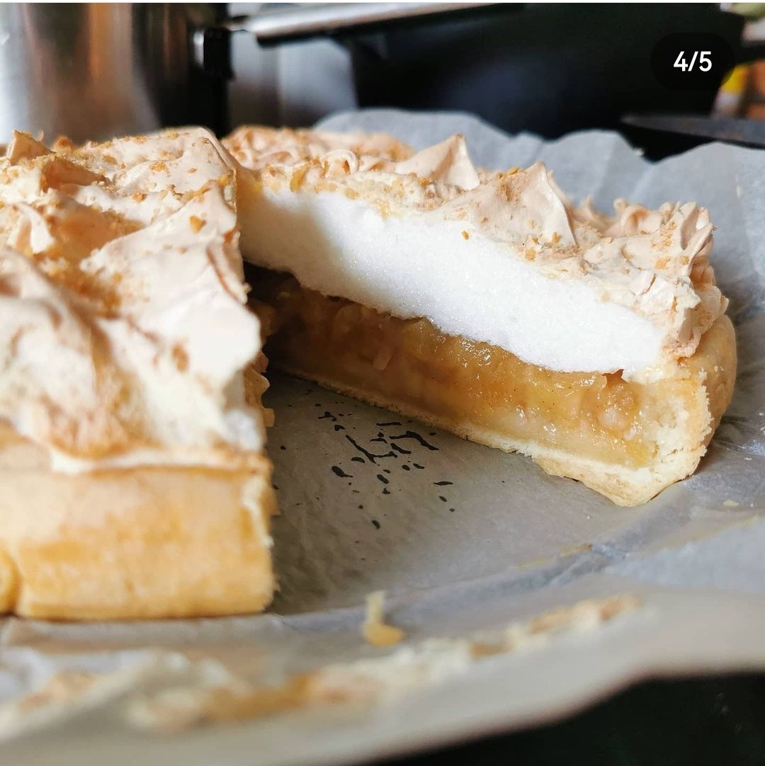 Kawałek domowego ciasta z jabłkami i bezą, widoczny przekrój z soczystym nadzieniem owocowym, beza z lekko przypieczonymi brzegami, ułożone na papierze do pieczenia.