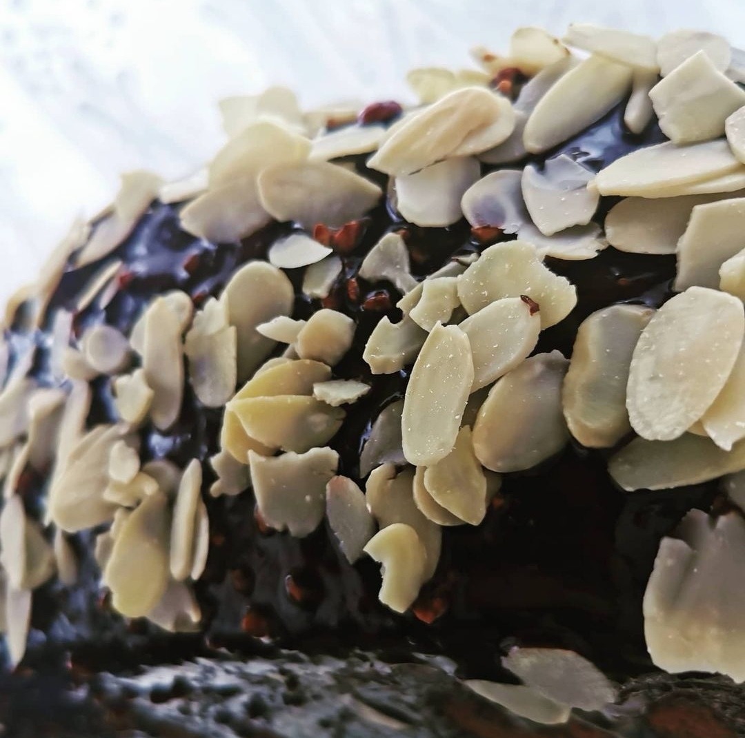 Czekoladowy tort udekorowany płatkami migdałów i posypką z orzechów laskowych, sfotografowany z bliska pod kątem, ukazujący fakturę polewy i migdałów.