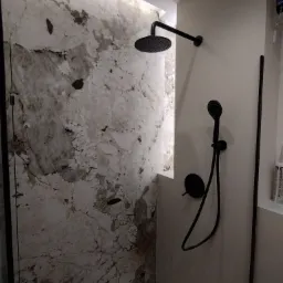 Nowoczesna kabina prysznicowa z czarną armaturą i ścianą wyłożoną płytami imitującymi marmur o nieregularnym wzorze.