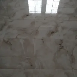 Jasne, marmurkowe płytki podłogowe z widocznym odbiciem okna, ułożone w regularny wzór.