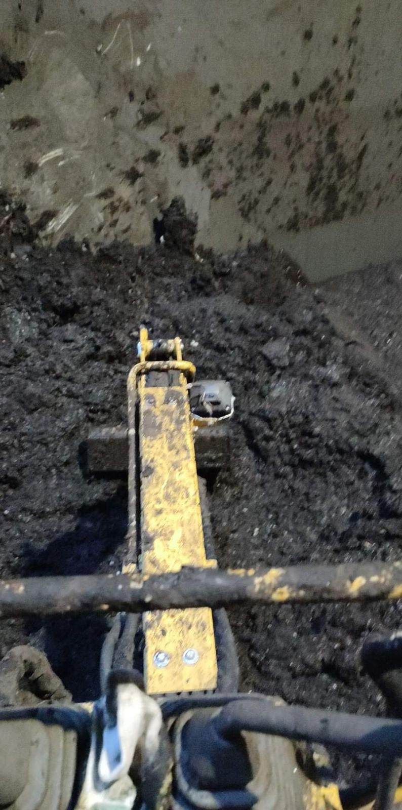 Żółty podnośnik hydrauliczny przytwierdzony do ściany pokrytej ciemnym, zwartym brudem, prawdopodobnie w trakcie prac wysokościowych.