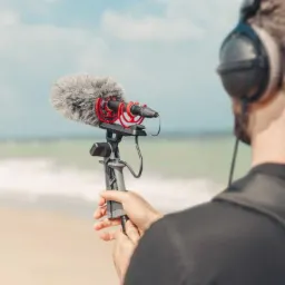 Osoba z mikrofonem kierunkowym i słuchawkami nagrywa dźwięk helikoptera na plaży.