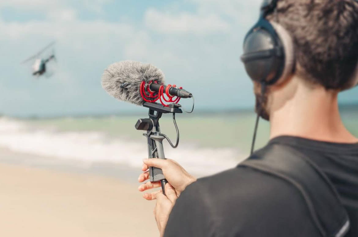 Osoba z mikrofonem kierunkowym i słuchawkami nagrywa dźwięk helikoptera na plaży.