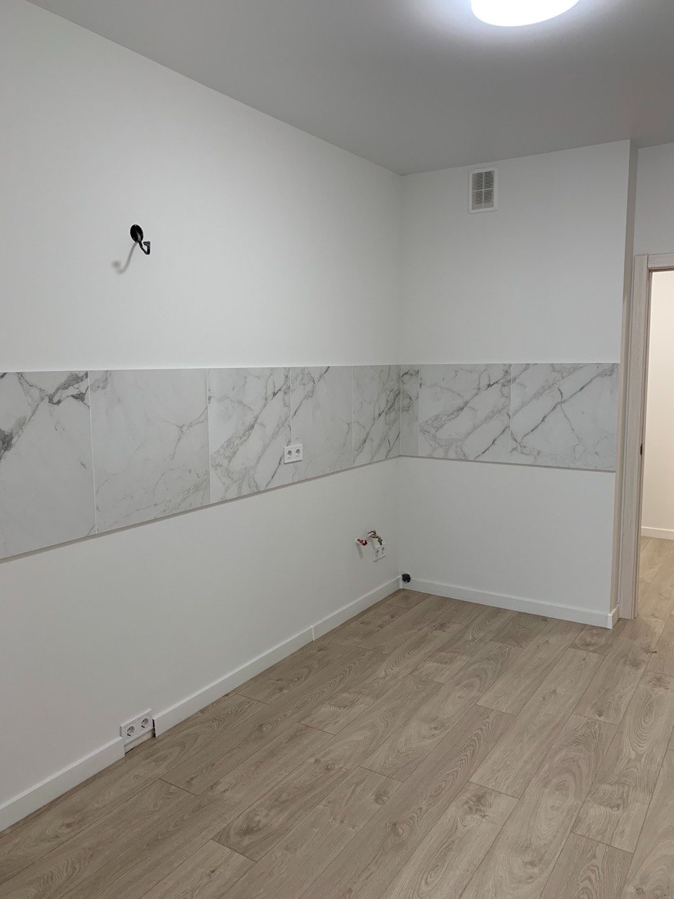 Wnętrze pokoju w Krakowie po remoncie, z położonymi panelami podłogowymi i częściowo wykończonymi ścianami, na których widać białą farbę i marmurowe płytki na dole, a także gniazdka elektryczne.
