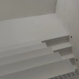 Nowoczesne schody wewnętrzne z białymi stopniami i marmurową posadzką, widok od dołu, z widocznym oświetleniem sufitowym.